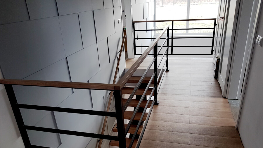 Metalowe schody wewnętrzne do domu z metalową balustradą i drewnianą poręczą